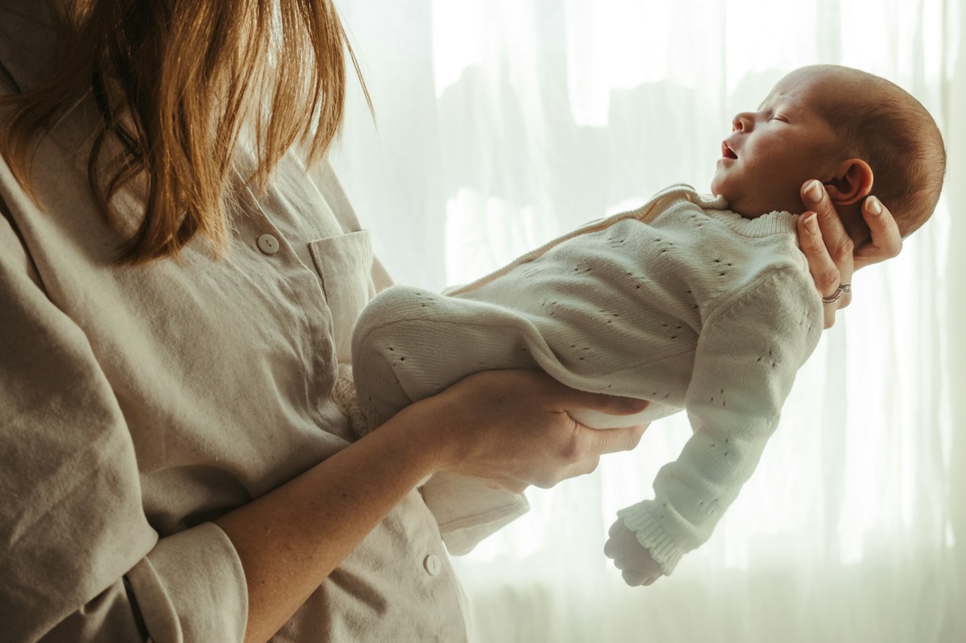 A mother holding her sleeping newborn by a sunlit window.