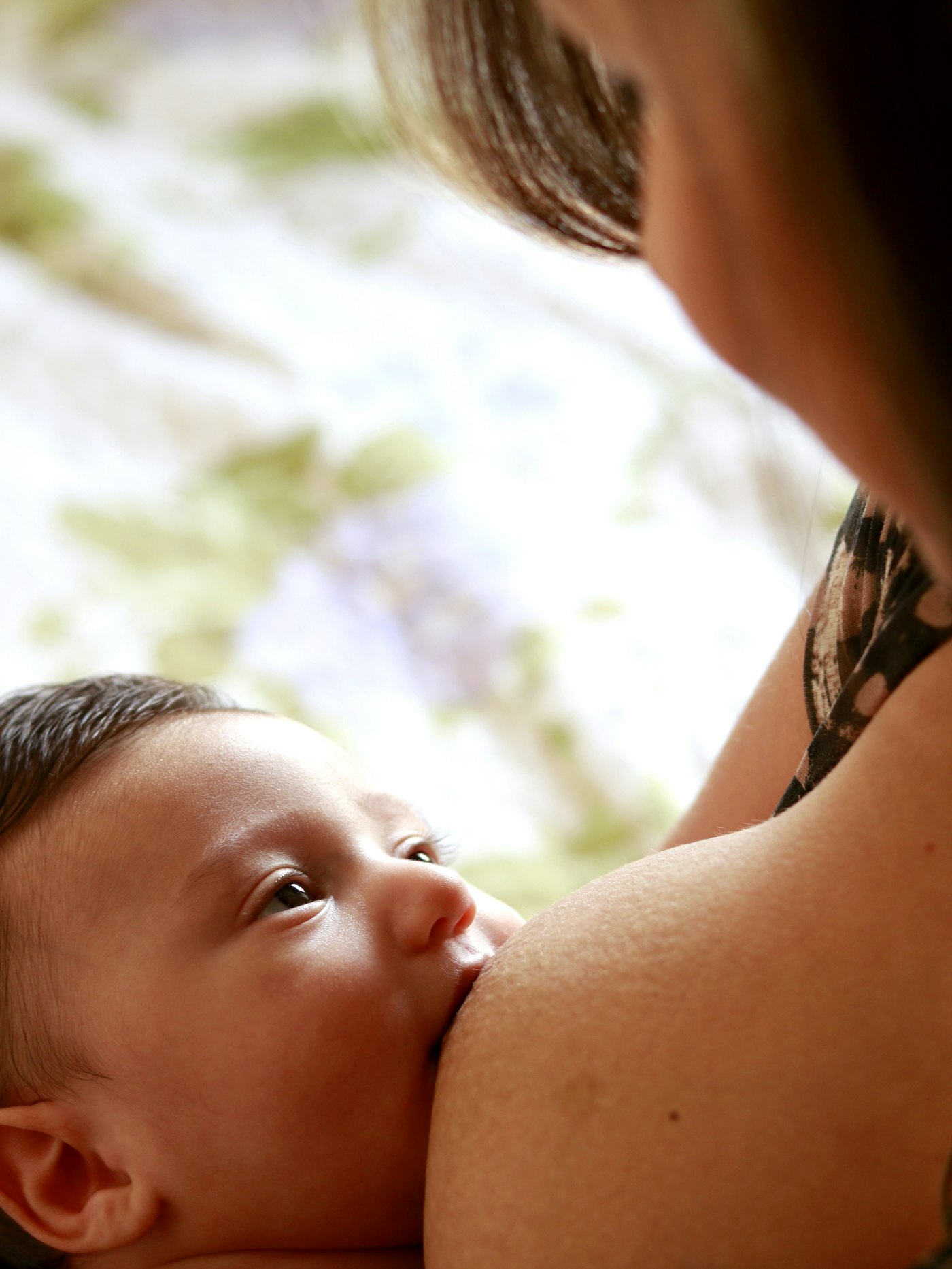 A close view of a baby breastfeeding and looking up at their mother.