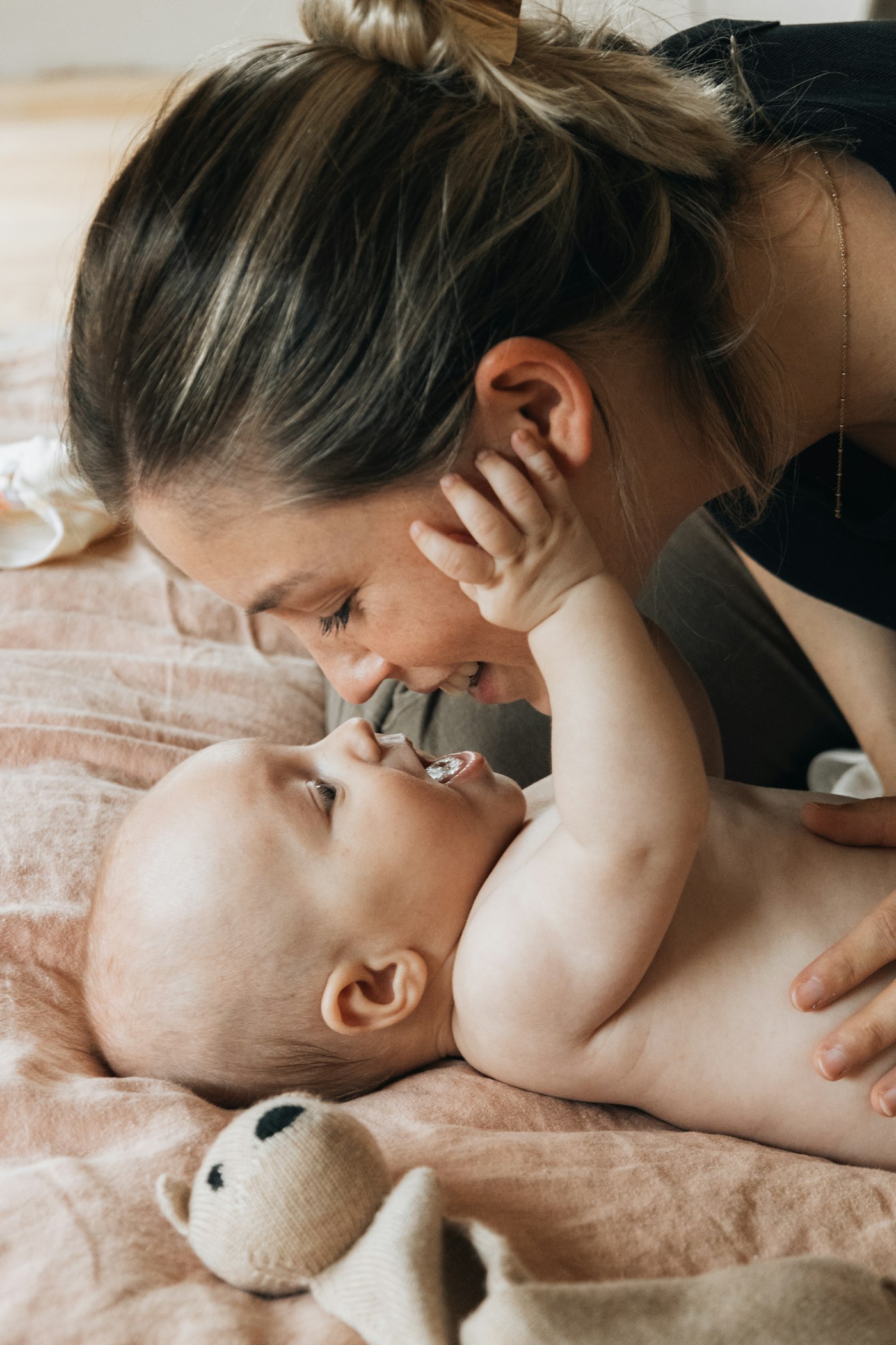 A mother leaning in nose to nose with her baby on a bed.
