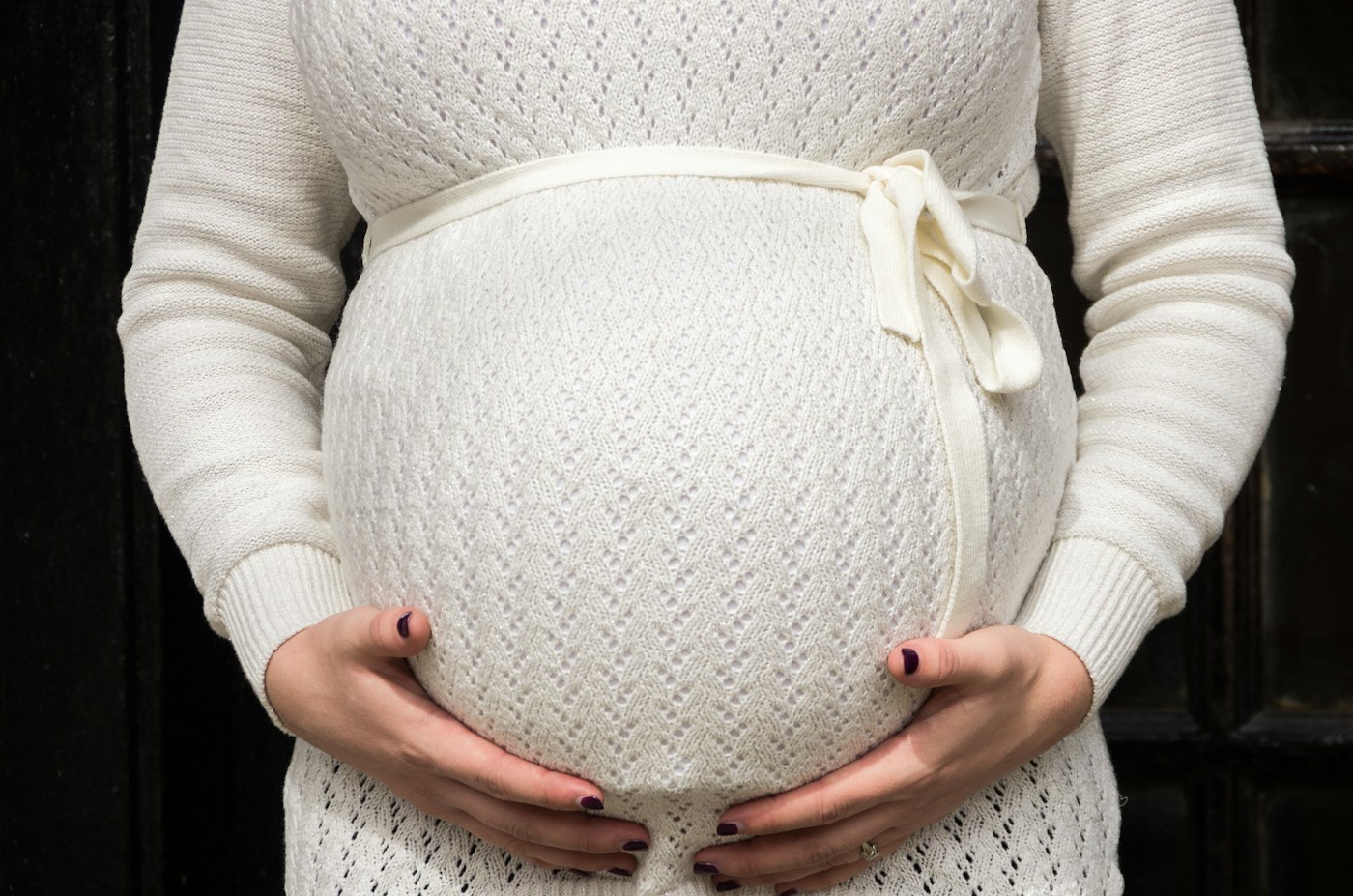 A pregnant woman in a cream sweater holding her belly.