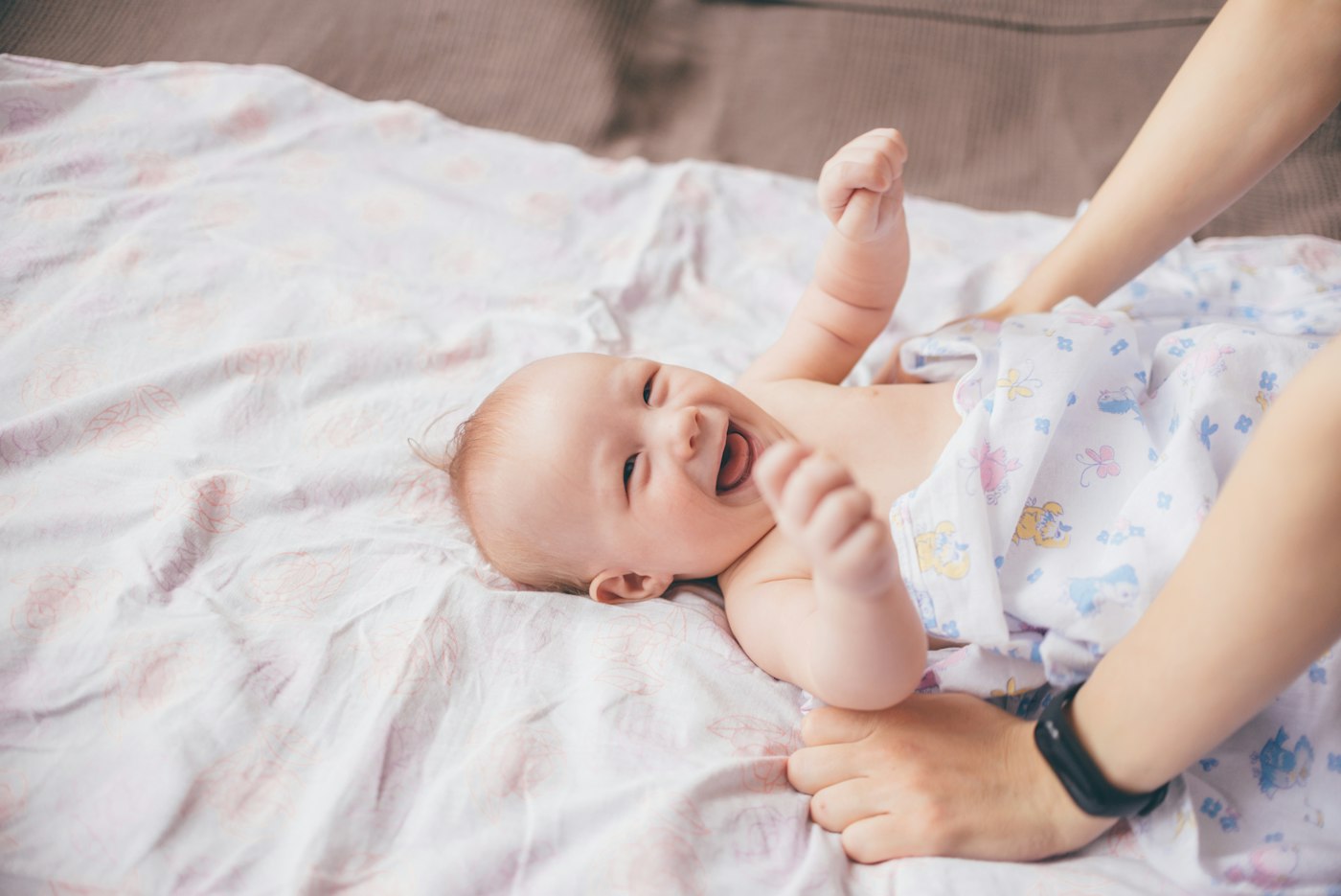 A laughing baby lying on a soft blanket at home.