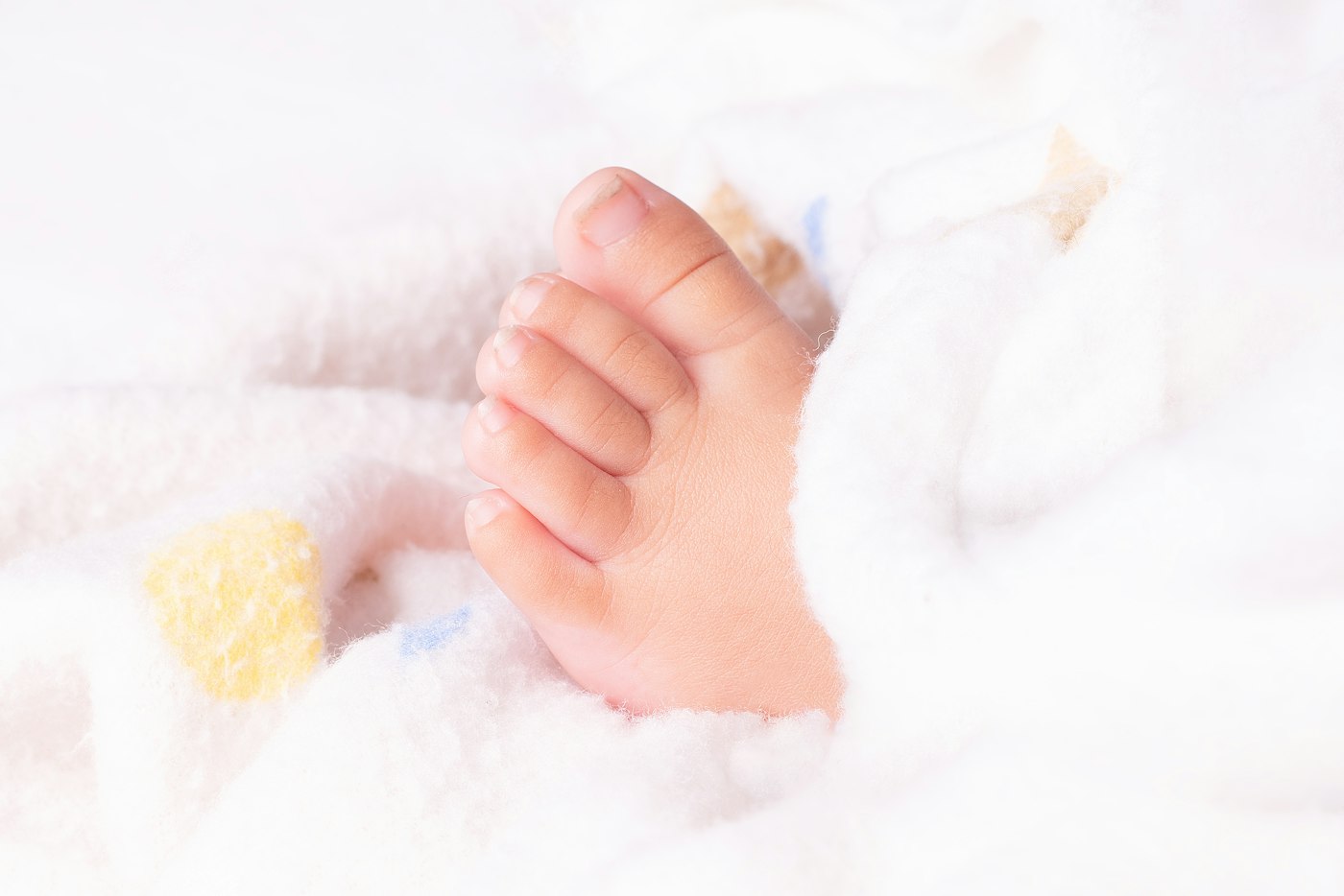 A newborn’s foot peeking out of a soft white blanket.